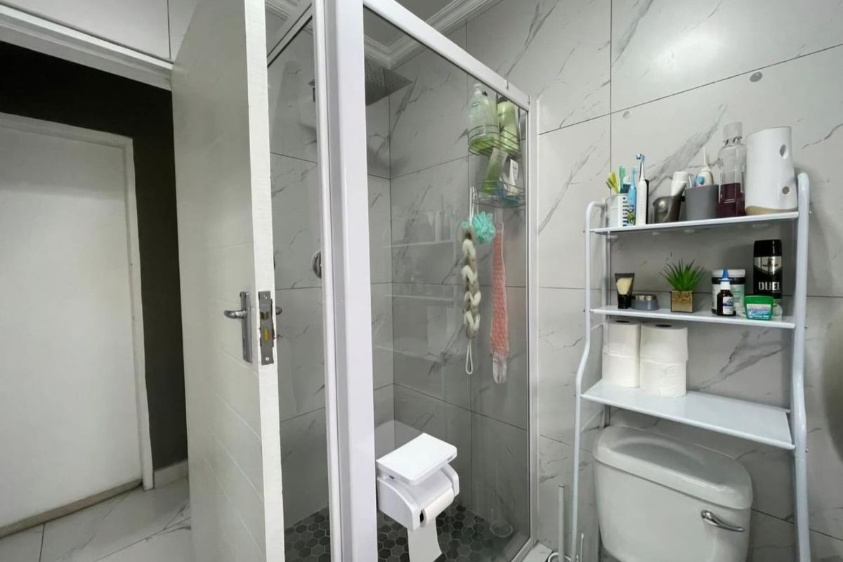 A modern bathroom featuring marble-look wall tiles, a glass-enclosed shower with a rainfall showerhead, and a standard toilet.