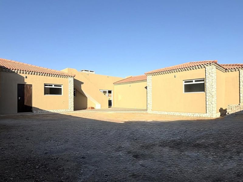 Rear view of the property featuring a paved courtyard, stone-clad accents, and terracotta roof tiles with an external staircase.