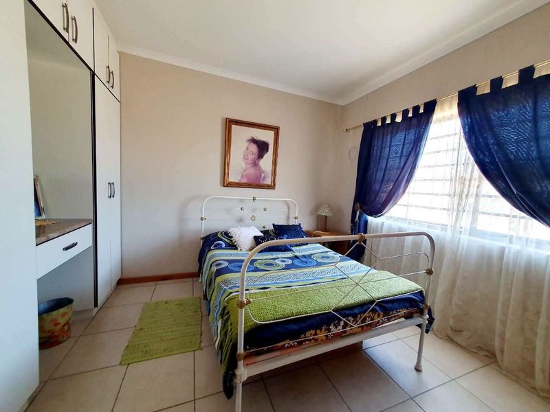 A functional bedroom featuring built-in cupboards, tiled flooring, and large windows with security bars, offering a practical and well-lit living space.