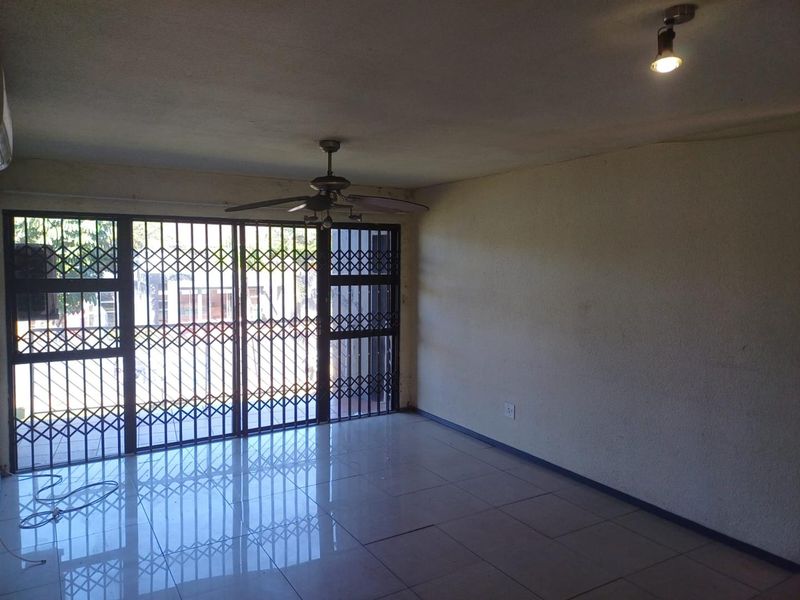 An empty living room featuring tiled flooring, a ceiling fan, and a large sliding door with a security gate leading to the exterior.