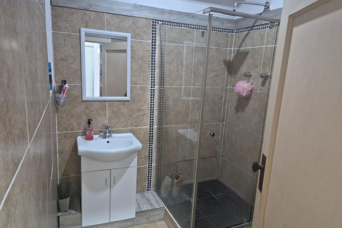 A functional bathroom featuring a vanity cabinet with a basin, a glass-enclosed shower, and neutral-toned wall and floor tiling.