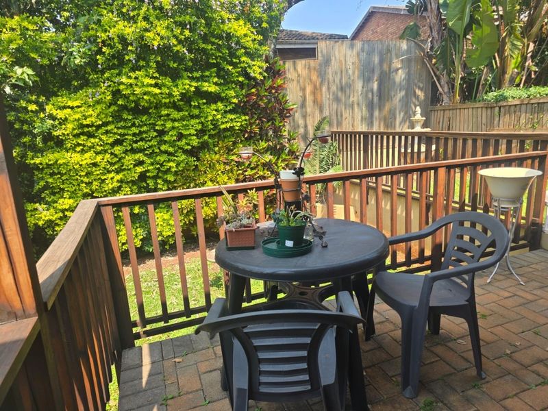 A raised outdoor patio area featuring paved flooring and a timber balustrade, overlooking a private garden space.