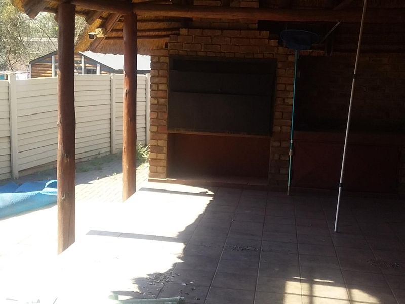 Covered outdoor patio area featuring a built-in brick braai, thatched roof, and tiled flooring, providing a functional space for outdoor entertaining.