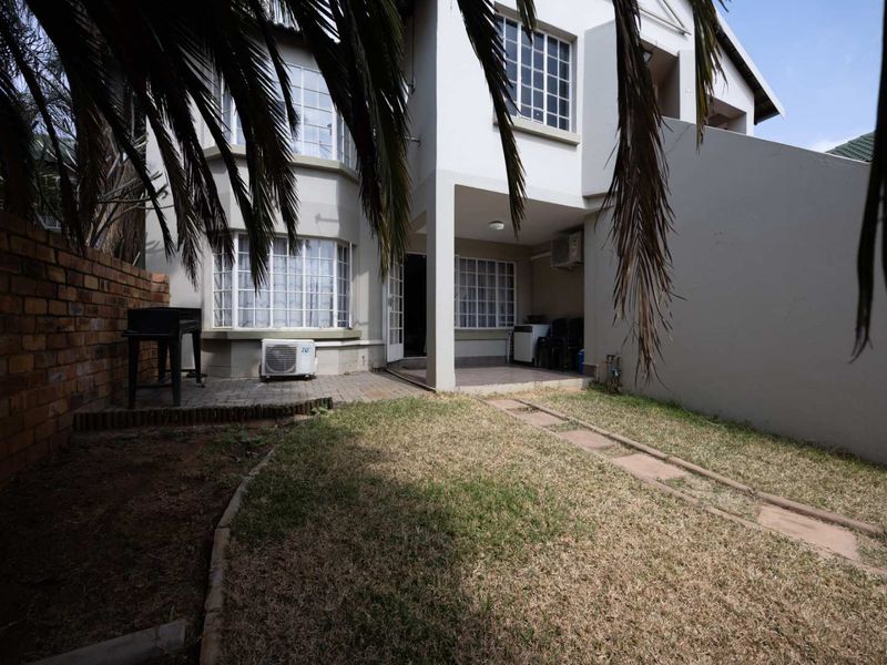 Rear exterior view of the apartment featuring a small private garden, paved patio area, and brick boundary wall.