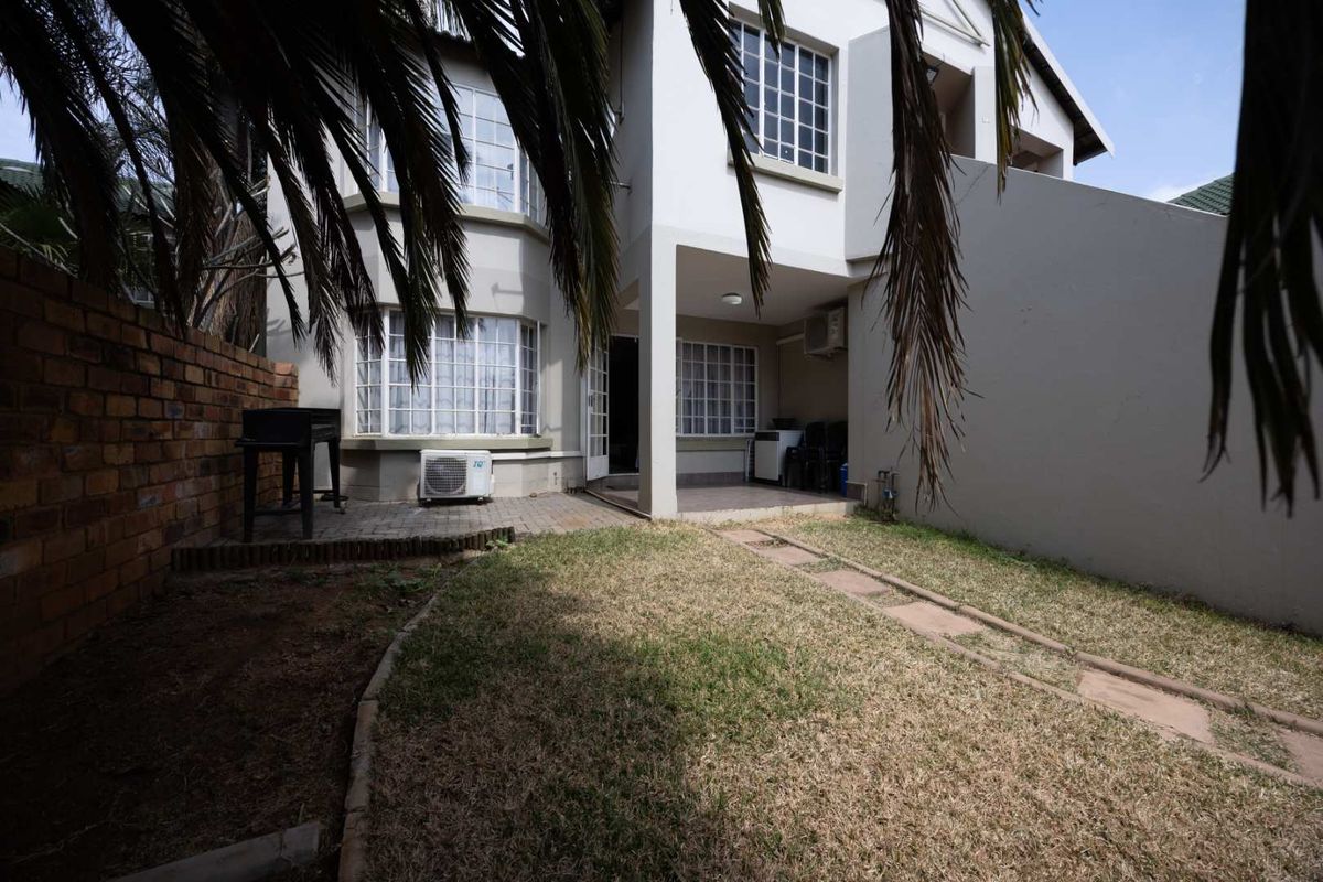 Rear exterior view of the apartment featuring a small private garden, paved patio area, and brick boundary wall.