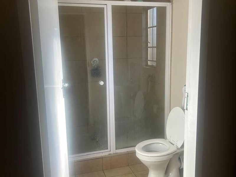 A functional bathroom featuring a shower enclosure, toilet, and tiled finishes throughout. The space is ready for a modern update.