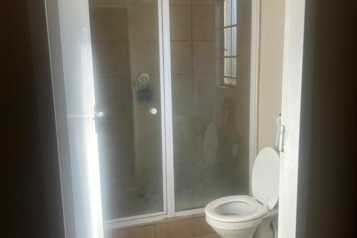 A functional bathroom featuring a shower enclosure, toilet, and tiled finishes throughout. The space is ready for a modern update.