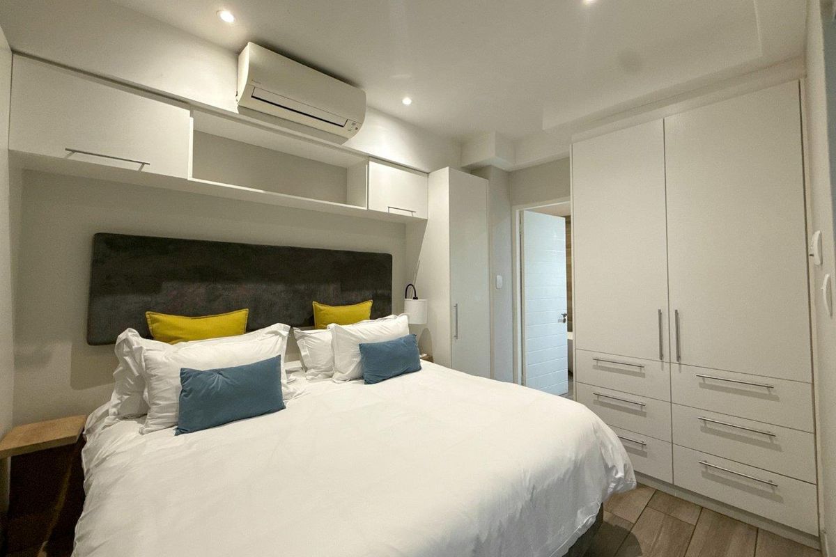 A well-maintained bedroom featuring built-in cupboards, overhead storage, split-system air conditioning, and modern recessed lighting.