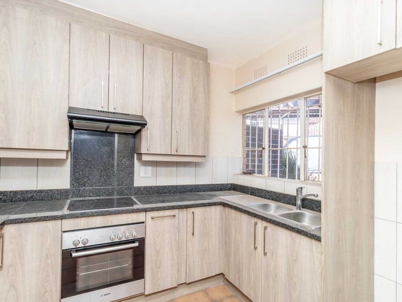 A functional kitchen featuring light wood-tone cabinetry, granite countertops, a built-in oven with electric hob, and a double stainless steel sink.