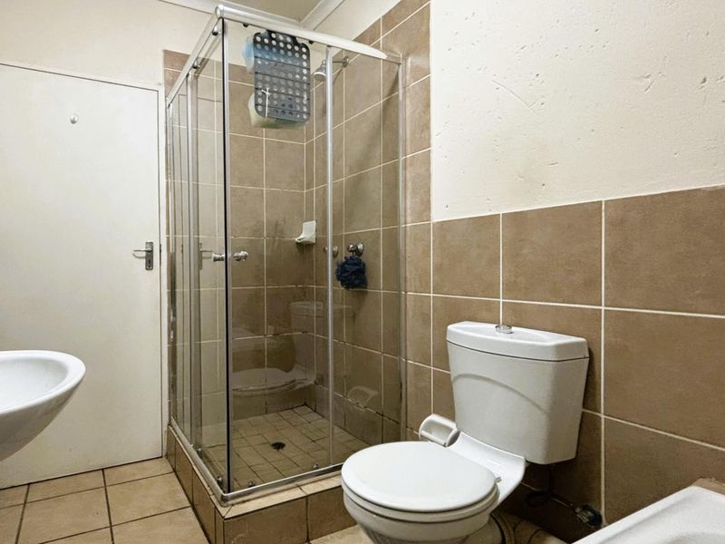 A functional bathroom featuring a glass shower enclosure, pedestal basin, and toilet with neutral wall and floor tiling.