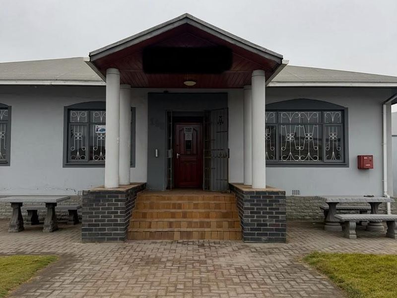 Front elevation of an office building featuring a covered entrance porch, brick pillars, security window bars, and a paved approach.