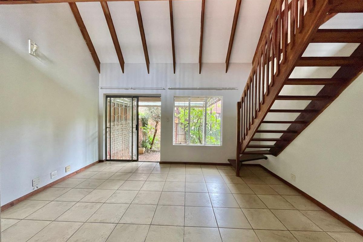 Spacious living area featuring vaulted ceilings with exposed timber beams, tiled flooring, and a wooden staircase leading to the upper level.