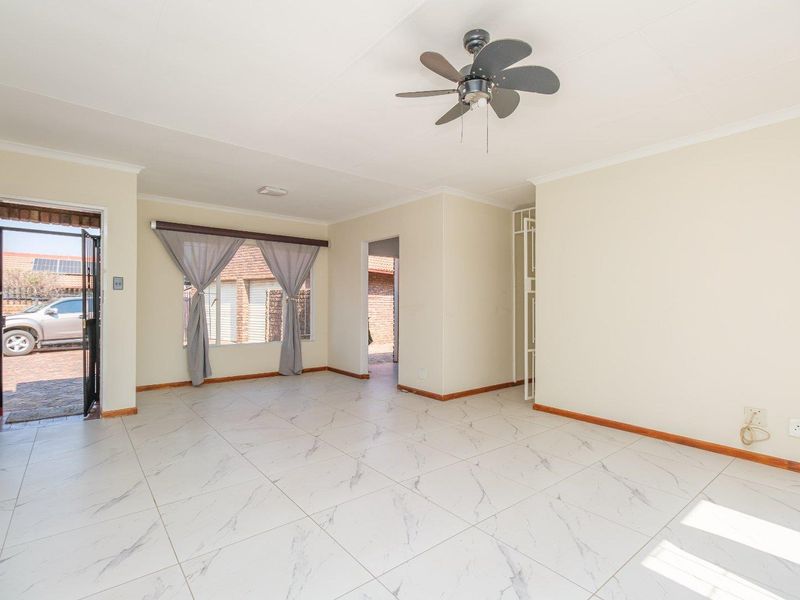 A bright, open-plan living area featuring neutral tiled flooring, a ceiling fan, and direct access to the exterior through a security gate.