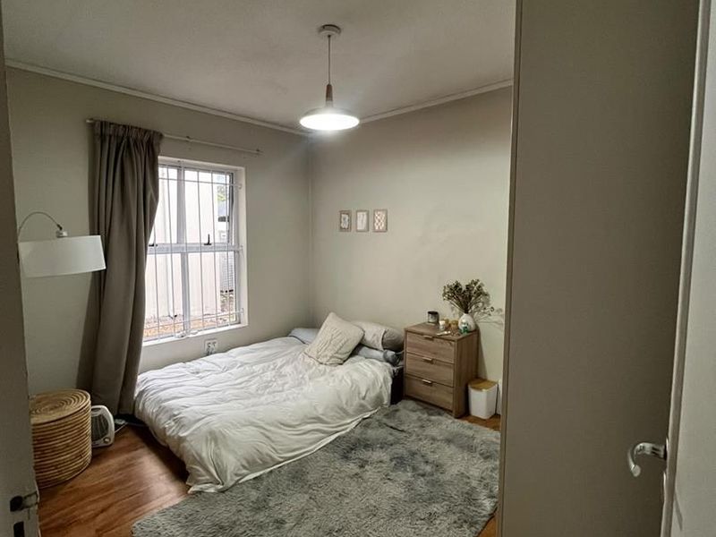 A cozy bedroom featuring laminate flooring, a window with security bars, and a central pendant light fixture.