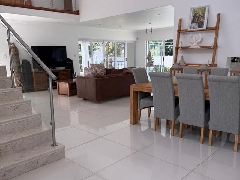 Spacious open-plan living and dining area featuring high ceilings, polished porcelain flooring, and a modern marble staircase with a glass balustrade.