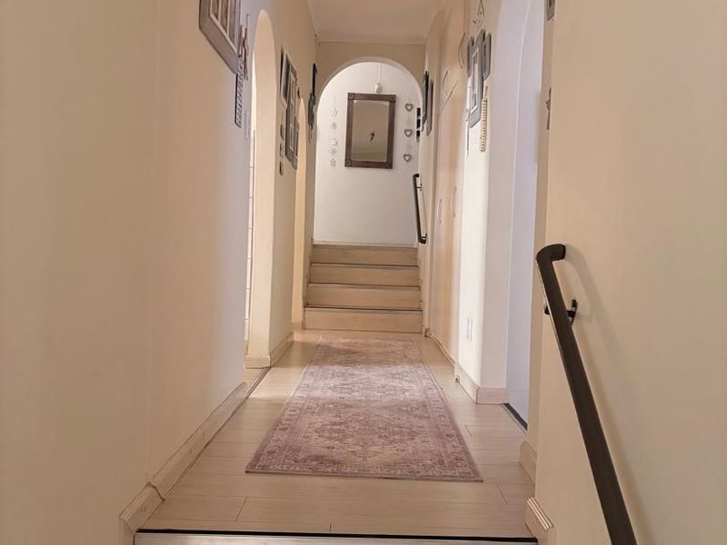 A bright hallway featuring arched doorways, a staircase with a handrail, and light-toned tiled flooring leading to an upper level.