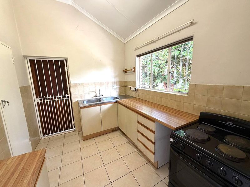 A functional kitchen featuring tiled flooring, laminate countertops, double sink, and built-in cabinetry with a vaulted ceiling and security gate access.