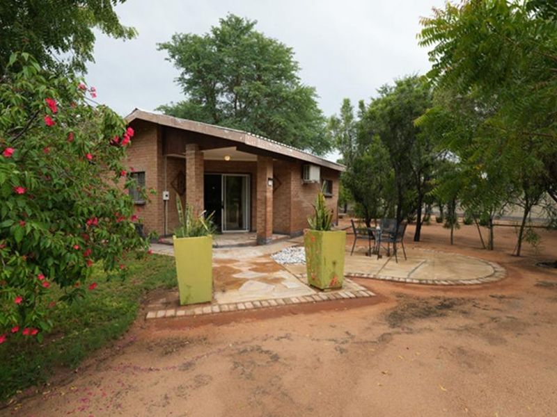 A rear view of a brick farmhouse featuring a covered patio area, sliding glass door access, and established garden surroundings.
