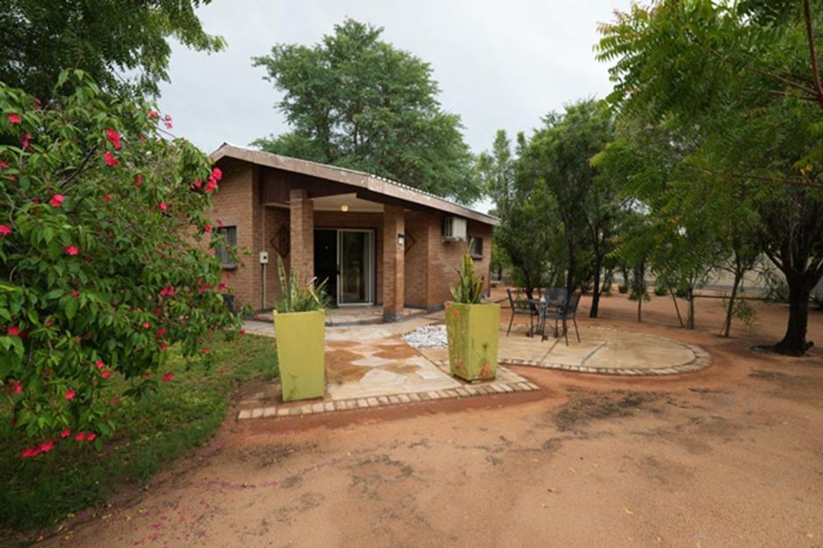 A rear view of a brick farmhouse featuring a covered patio area, sliding glass door access, and established garden surroundings.