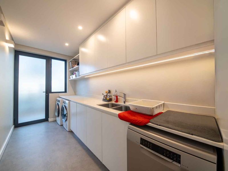 Modern, well-lit laundry room featuring sleek white cabinetry, integrated sink, and direct access to an outdoor area.