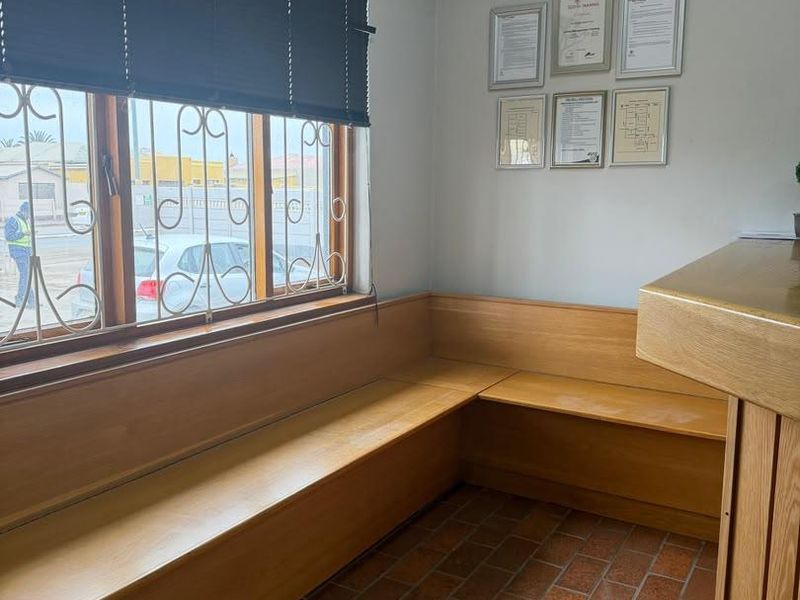 A professional office reception area featuring built-in wooden bench seating, terracotta tile flooring, and security-fitted windows with venetian blinds.
