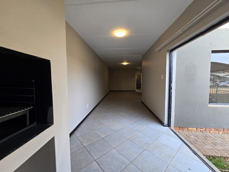 A spacious covered patio area featuring tiled flooring, a built-in braai, and direct access to the exterior through a sliding door.