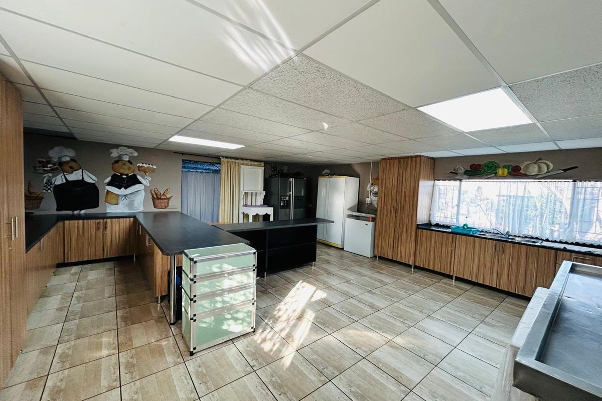 Spacious kitchen featuring extensive wood-grain cabinetry, dark countertops, tiled flooring, and a drop ceiling with integrated lighting.