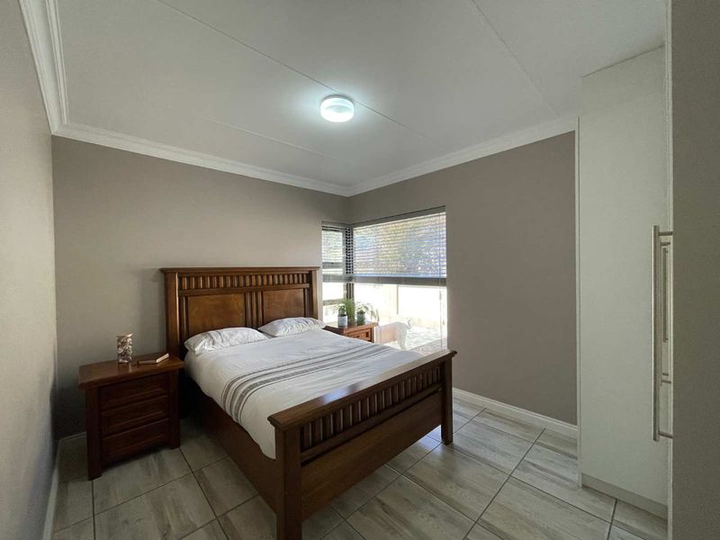 A well-maintained bedroom featuring neutral wall tones, tiled flooring, built-in cupboards, and a corner window with venetian blinds.