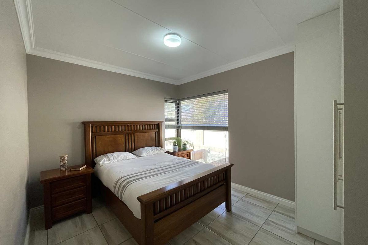 A well-maintained bedroom featuring neutral wall tones, tiled flooring, built-in cupboards, and a corner window with venetian blinds.