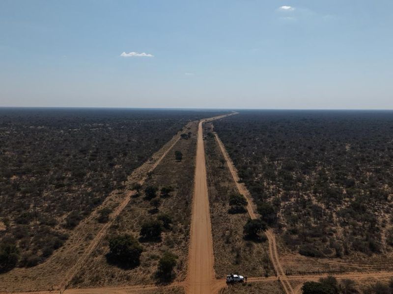 An aerial view of a long dirt road stretching through expansive, undeveloped farm land with natural vegetation.