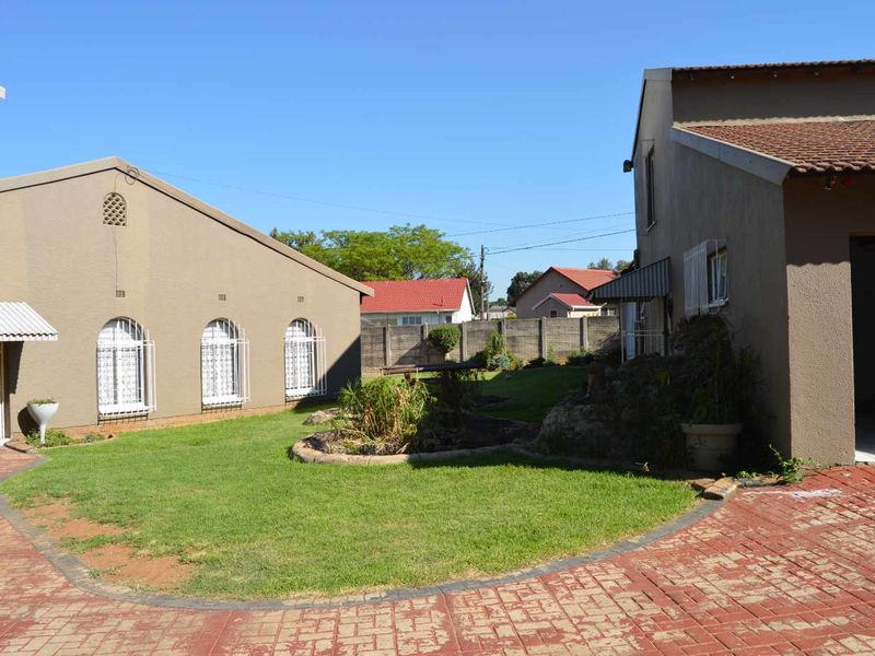 A view of the rear garden area featuring a paved driveway, well-maintained lawn, and secure building facades with tiled roofing.