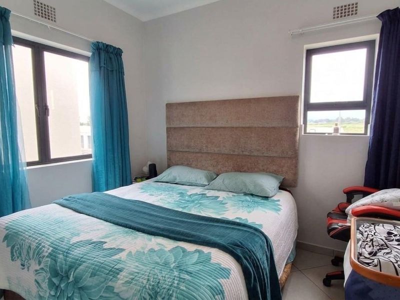 A functional bedroom featuring tiled flooring, neutral wall finishes, and aluminium-framed windows providing natural light.