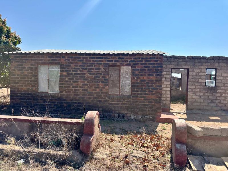 A single-story residential structure featuring exposed brick and concrete block construction with a corrugated metal roof, currently in need of significant maintenance and repair.
