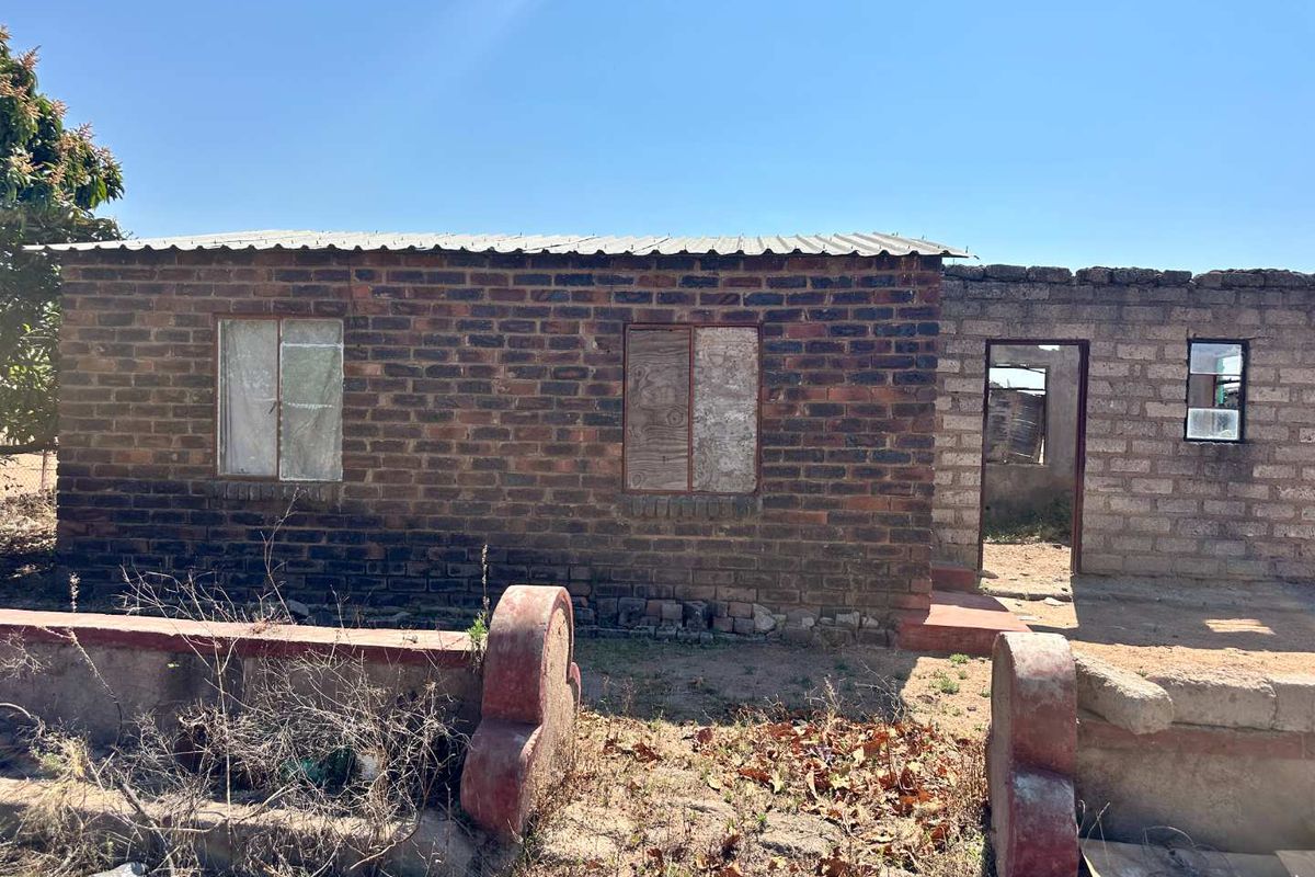 A single-story residential structure featuring exposed brick and concrete block construction with a corrugated metal roof, currently in need of significant maintenance and repair.