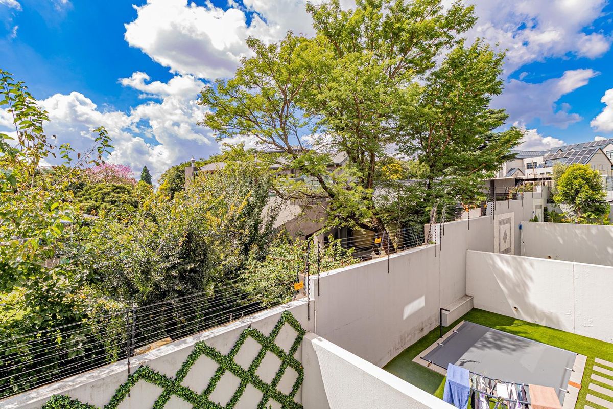 Elevated view of the rear courtyard area featuring a covered pool, perimeter wall with electric fencing, and established garden greenery.