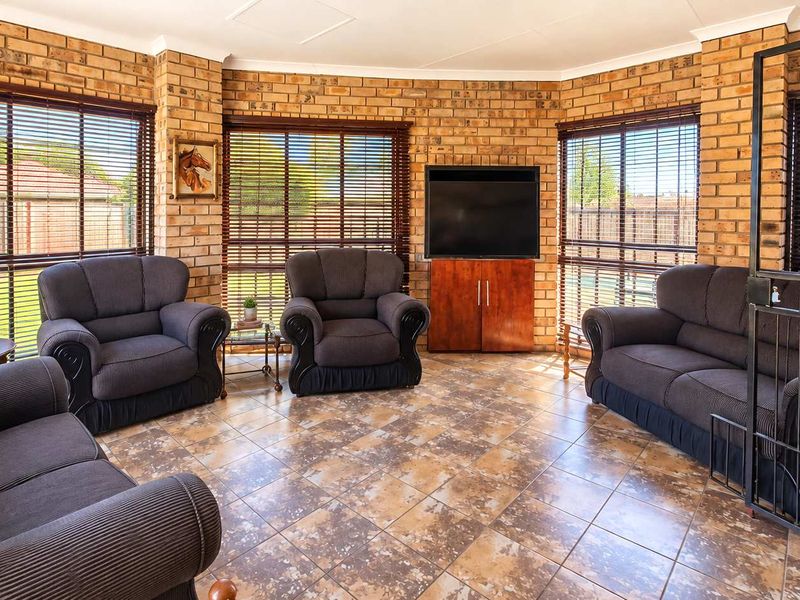 A living room featuring exposed brick walls, tiled flooring, and large windows with venetian blinds, providing a bright and textured living space.