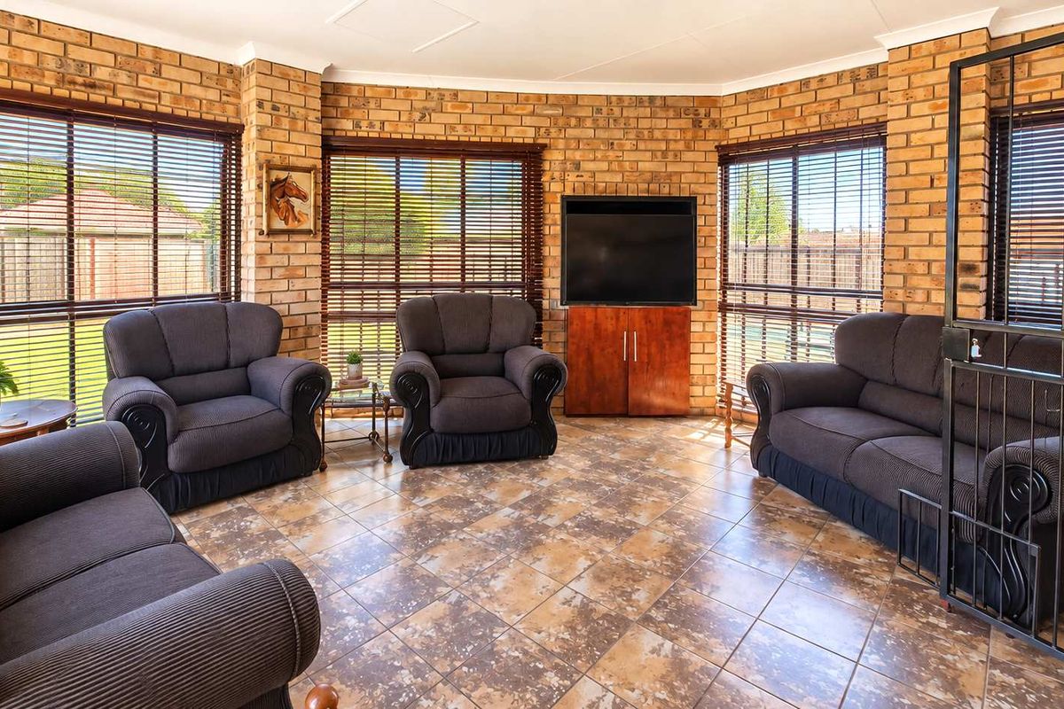 A living room featuring exposed brick walls, tiled flooring, and large windows with venetian blinds, providing a bright and textured living space.