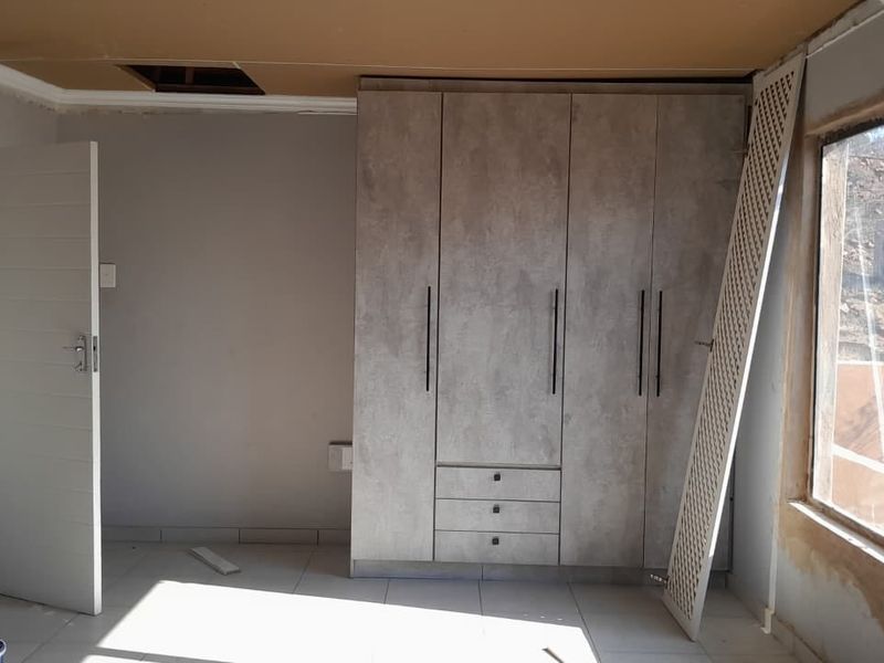 A bedroom featuring a modern built-in wardrobe and tiled flooring, currently undergoing renovation with unfinished ceiling and wall details.