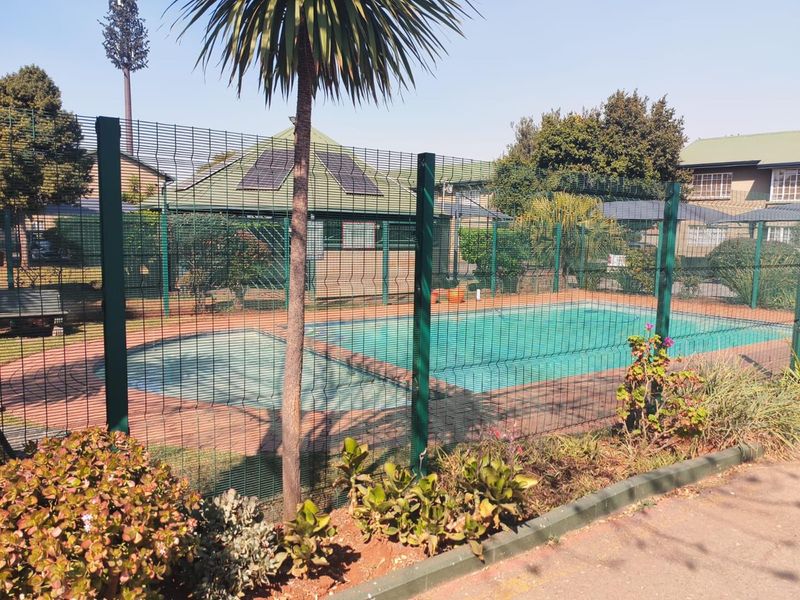 Communal swimming pool area featuring secure perimeter fencing, paved surrounds, and solar panels installed on the adjacent structure.