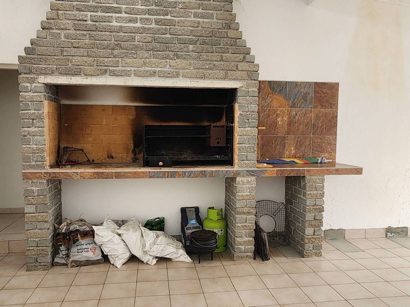 Covered patio area featuring a large built-in brick braai with tiled prep surfaces and ceramic floor tiling.