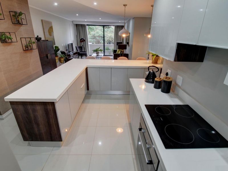 Modern open-plan kitchen featuring sleek white cabinetry, quartz countertops, and integrated appliances, flowing seamlessly into a bright living area with balcony access.