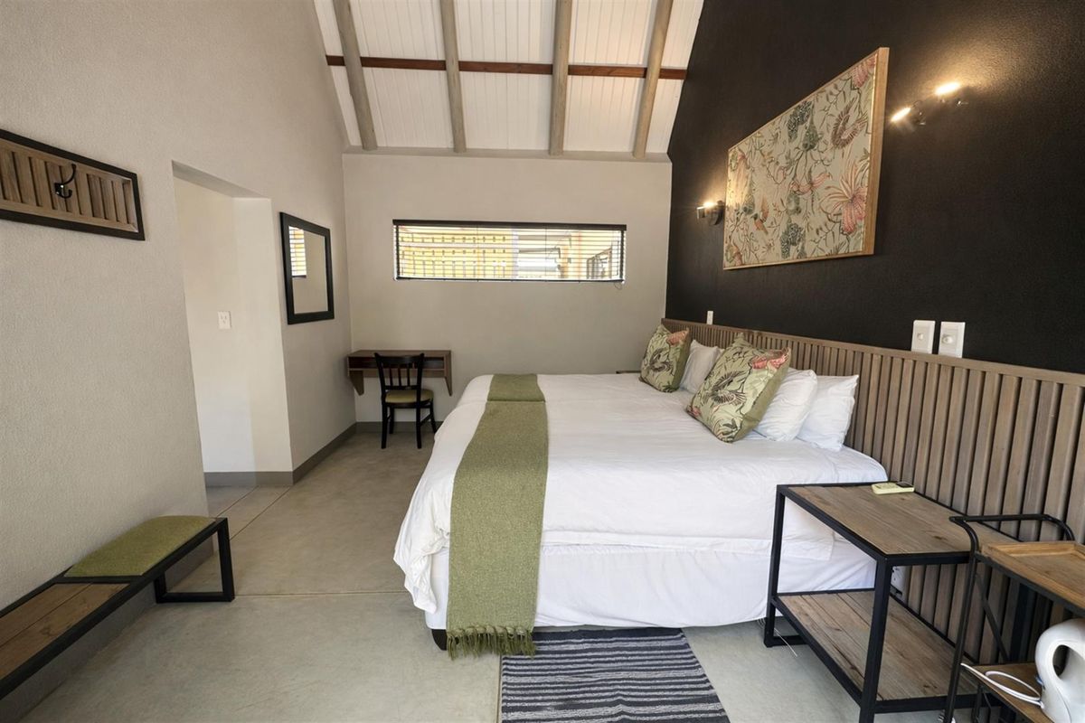 Spacious bedroom featuring a high vaulted ceiling with exposed beams, polished concrete flooring, and a modern timber-slatted headboard feature wall.