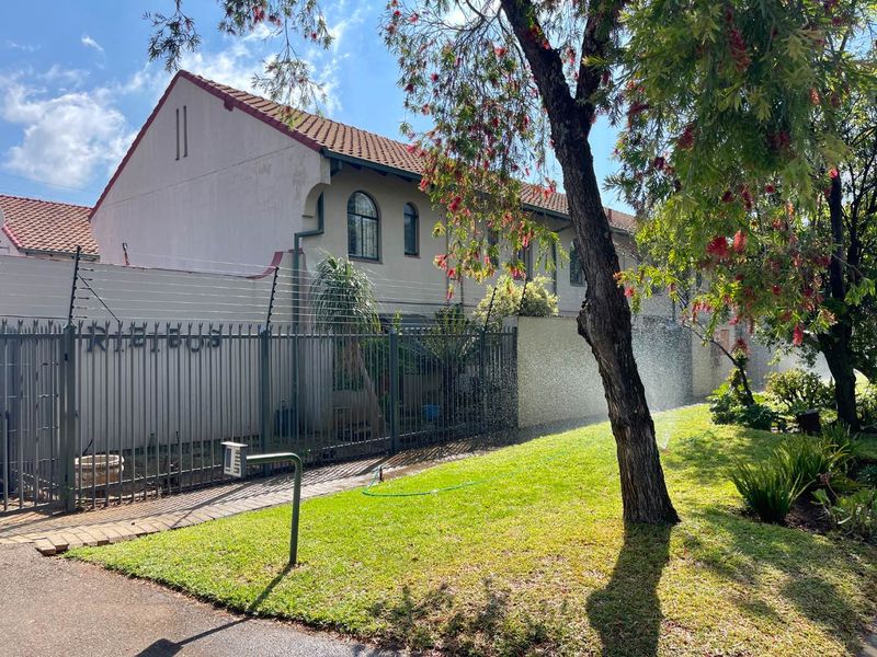 Front exterior view of the townhouse featuring a paved driveway, secure metal fencing with electric wires, and a well-maintained garden area.