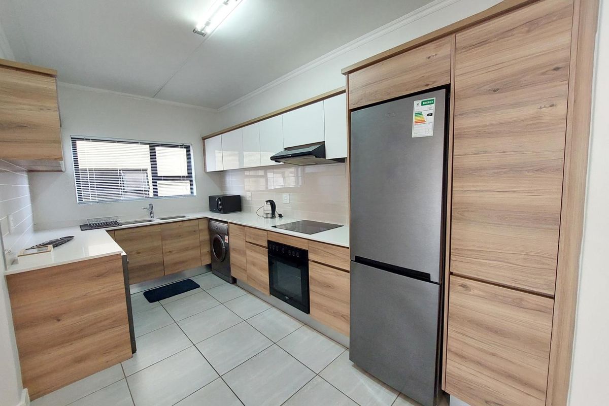 Modern kitchen featuring wood-grain cabinetry, stone countertops, integrated appliances, and tiled flooring, offering a clean and functional workspace.