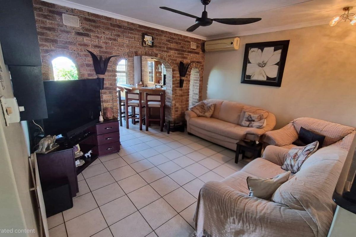A living room featuring exposed brick walls with arched architectural details, tiled flooring, a ceiling fan, and a wall-mounted air conditioning unit.