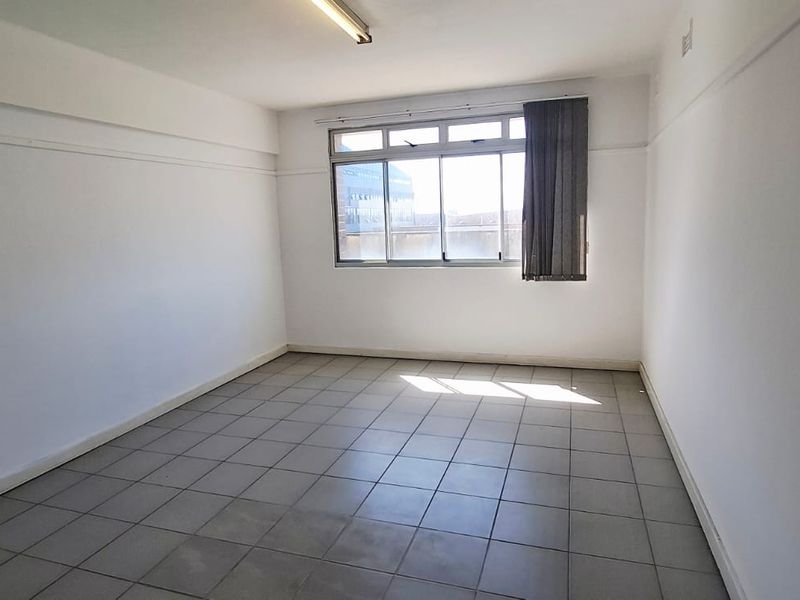 A vacant, neutrally painted office space featuring tiled flooring and large aluminium-framed windows, providing a blank canvas for professional use.
