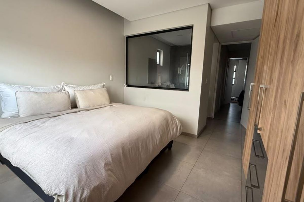 Modern bedroom featuring tiled flooring, a built-in wardrobe, and a unique internal glass partition looking into the adjacent bathroom area.