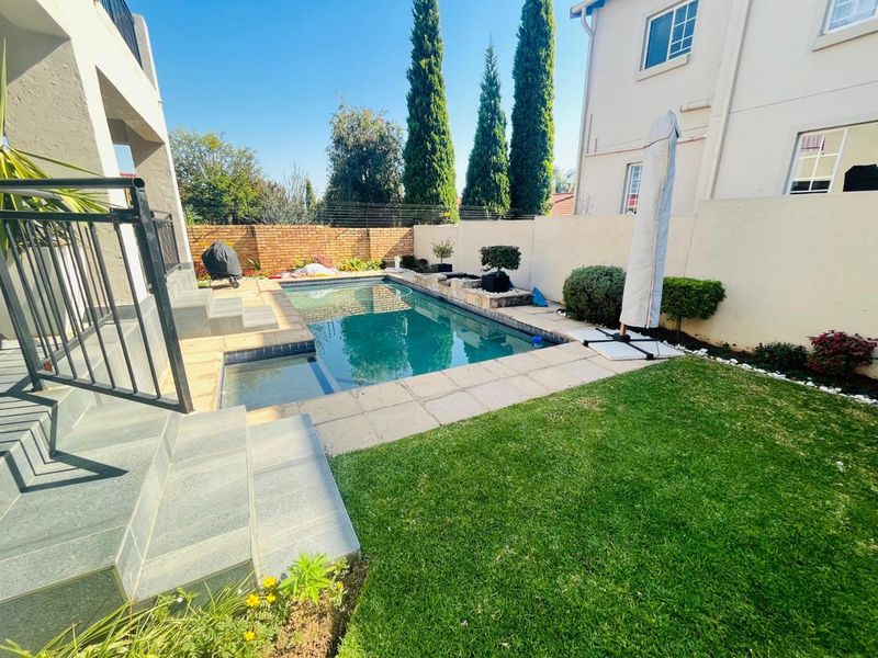A well-maintained outdoor pool area featuring a paved surround, manicured lawn, and secure brick boundary wall, perfect for relaxation and outdoor entertainment.