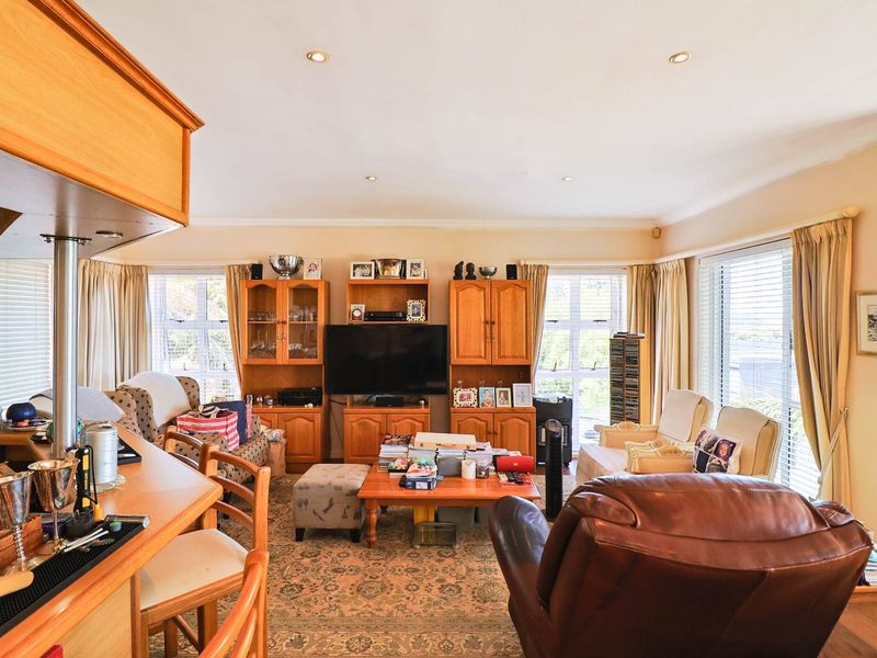 Spacious open-plan living area featuring a breakfast bar, built-in cabinetry, and large windows with venetian blinds, offering a functional and well-lit layout.