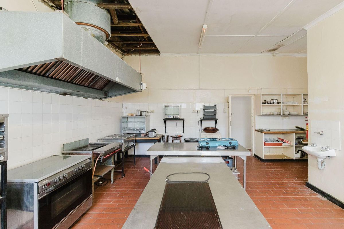 Commercial kitchen space featuring stainless steel prep tables, built-in oven, extractor hood, and tiled flooring, requiring significant ceiling and wall repairs.